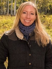 A woman with blonde hair standing with her hands in her jacket pockets