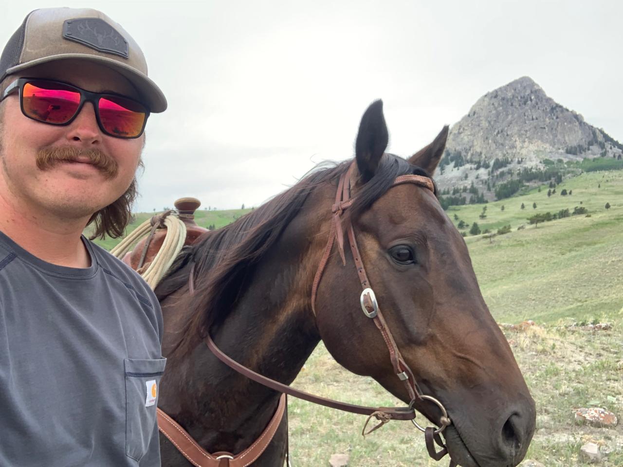 A man in baseball cap with mustache holding a horse on a rein