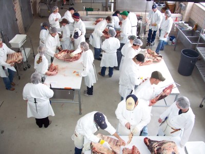 a group of meat scientists in white coats and food safety gear are learning cuts of meat