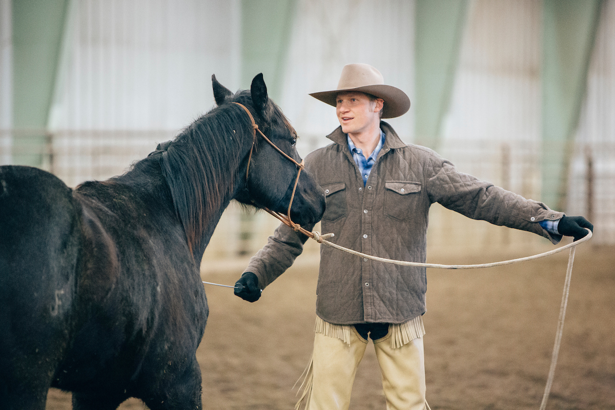 a young man in a hat with a horse on a lead